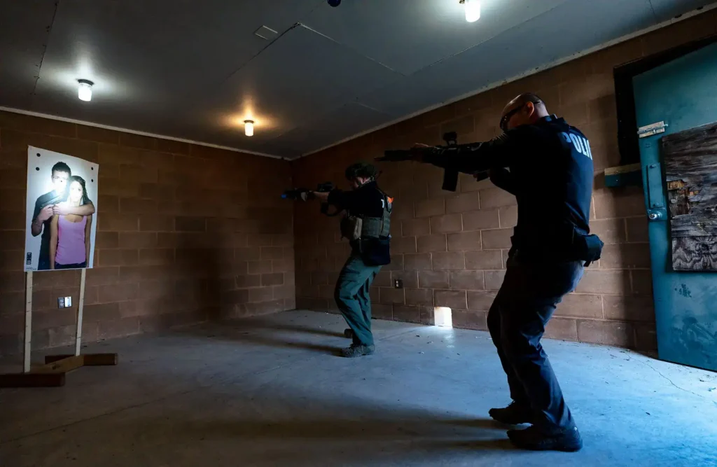 two officers in room aiming firearms at target