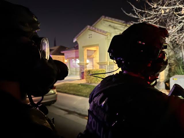 Floodlights illuminate a house during a SWAT barricade operation.